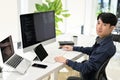 Professional Asian male programmer sits at his office desk, smiling at looking at the camera