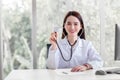 Professional Asian woman doctor wears medical coat and stethoscope in office room while looking at the camera at hospital with Royalty Free Stock Photo