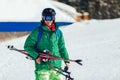 Professional athlete skier in an green jacket wearing a black mask and holding skis