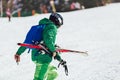 Professional athlete skier in an green jacket wearing a black mask and holding skis Royalty Free Stock Photo