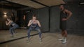 Sporty fit female fitness instructor showing curtsy lunges exercise to man