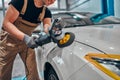 Professional auto detailer hand holding rotary polisher while polishing paint surface of shiny white car