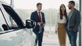 Professional automobile seller in suit is having conversation with attractive rich couple telling them about new car Royalty Free Stock Photo