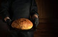 Professional baker holds in his hands freshly baked bread on a sheet pan in the bakery. Presentation of bakery products. Place for