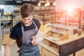 Professional caucasian bakery owner in grey apron holding grissini and smiling inviting guests to own bakery shop