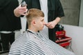 Professional barber cuts the hair of a young blond man in a wig, the client sits with a calm face in a barber shop and looks away Royalty Free Stock Photo