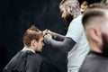 Professional tattooed barber using cutthroat razor cutting hair. Attractive male is getting a modern haircut in barber