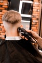 Professional barber using an electric shaver or trimmer to neaten the modern V-shaped hairstyle of a male customer Royalty Free Stock Photo