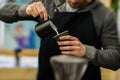 Professional barista in coffee house pouring frothed milk into paper cup for cappuccino. Coffee culture and professional