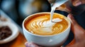 Professional barista pouring a steamed milk into a coffee cup making a latte art, closeup. Freshly brewed coffee with latte art in