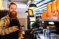 Professional barista young redhaired ginger bearded man in black apron working in coffee shop