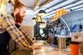 Professional barista young redhaired ginger bearded man in black apron working in coffee shop
