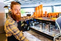 Professional barista young redhaired ginger bearded man in black apron working in coffee shop