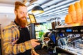 Professional barista young redhaired ginger bearded man in black apron working in coffee shop