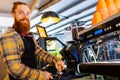 Professional barista young redhaired ginger bearded man in black apron working in coffee shop