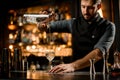 Professional bartender with a beard pouring alcoholic drink from the measuring cup to the glass through the strainer