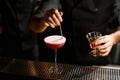 Professional bartender decorated a pink cocktail the a white scum with a liquor on the toothpick