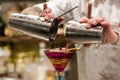 Professional bartender pouring cocktail from the shaker into the glass. Barman holding in hands cocktail tool.