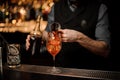 Professional bartender pouring a delicious cocktail from the steel jigger