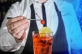 A professional bartender puts a cherry in a red chilled alcoholic cocktail with bar tweezers in glass at a nightclub counter