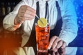 A professional bartender puts a slice of lemon in a red chilled alcoholic cocktail with bar tweezers in glass at a nightclub