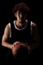 Professional basketball player holding a ball against black background. Serious concentrated african american man in sports