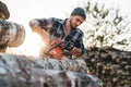 Professional bearded strong lumberman wearing plaid shirt sawing tree with chainsaw for work Royalty Free Stock Photo