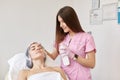 Professional beautician puts on face of client chemical peeling agent. Cosmetologist holds big bottle of cream, attractive woman Royalty Free Stock Photo
