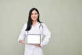 Professional Asian female doctor holding tablet mockup, standing against grey background Royalty Free Stock Photo