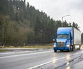 Professional big rig blue semi truck tractor transporting commercial cargo in dry van semi trailer running on the evening wet Royalty Free Stock Photo