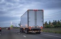 Professional big rig semi truck with dry van semi trailer running on the night highway road with turn on light Royalty Free Stock Photo