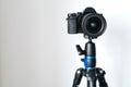 Professional black mirrorless camera stands on a tripod against a white wall. Royalty Free Stock Photo