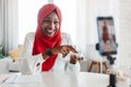 Professional black muslim beauty blogger advertising skincare cosmetics, talking to smartphone on tripod Royalty Free Stock Photo