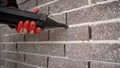 Professional builder filling fugue with grout gun near brick wall, closeup. Tiles installation process. Grouting with a