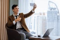 Professional businessman taking selfie near window with skyscraper. Ornamented. Royalty Free Stock Photo