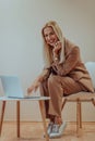 A professional businesswoman sits on a chair, surrounded by a serene beige background, diligently working on her laptop Royalty Free Stock Photo