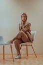 A professional businesswoman sits on a chair, surrounded by a serene beige background, diligently working on her laptop Royalty Free Stock Photo