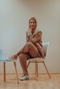 A professional businesswoman sits on a chair, surrounded by a serene beige background, diligently working on her laptop Royalty Free Stock Photo