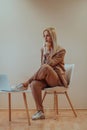 A professional businesswoman sits on a chair, surrounded by a serene beige background, diligently working on her laptop Royalty Free Stock Photo