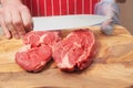 Professional butcher holding wooden cutting board with two rib eye steaks. Left hand in plastic blue glove, right hand holding