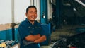 Professional car mechanic looking at camera and smiling at repair service station. Skillful Asian guy in uniform fixing car at Royalty Free Stock Photo