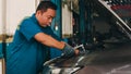 Professional car mechanic screwing details of car engine on lifted automobile at repair service station. Skillful Asian guy in Royalty Free Stock Photo