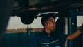 Professional car mechanic using paperwork makes the oil and engine check to the car on lifted automobile at repair service station