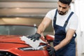 Professional car wash worker holding the gray microfiber and polishing the car hood