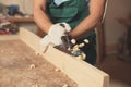 Professional carpenter grinding plank with jack plane in workshop, closeup