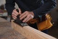 Professional carpenter grinding wooden plank with jack plane in workshop