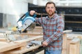 Professional carpenter using sawing machine for cutting wooden board at sawmill. Skilled cabinet maker working with Royalty Free Stock Photo