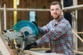 Professional carpenter using sawing machine for cutting wooden board at sawmill. Skilled cabinet maker working with Royalty Free Stock Photo