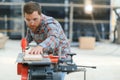 Professional carpenter using sawing machine for cutting wooden board at sawmill. Skilled cabinet maker working with Royalty Free Stock Photo