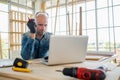 Professional carpenter wear glove sitting on the chair and hold pencil and looking at laptop. Working in the modern wood workplace